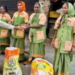 Sanitation workers in uniform receiving dry ration packets during a community support drive.