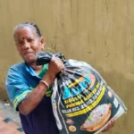 Elderly woman in India carrying a donated rice bag as part of early relief work.